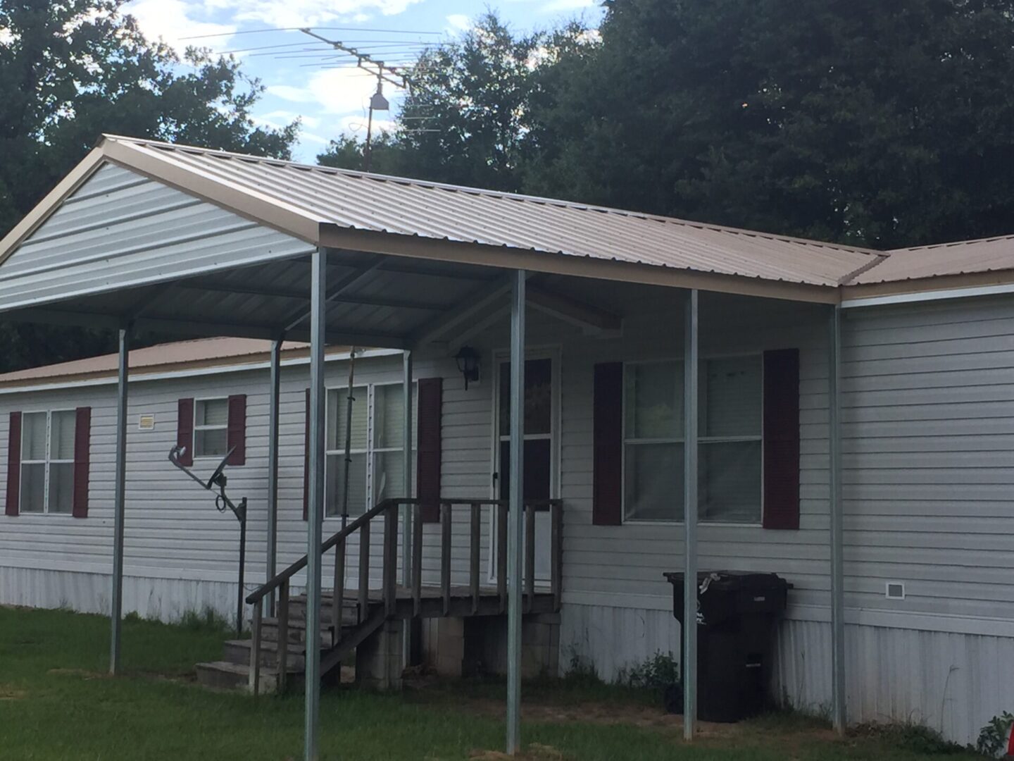 Small house with a simple porch and stairs, surrounded by greenery.